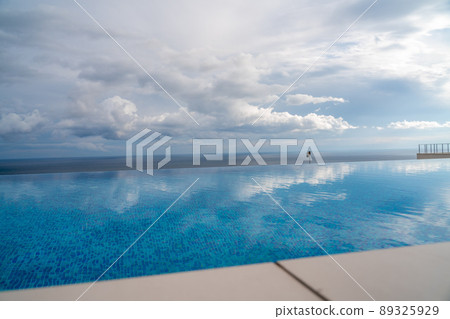 Infinity pool with sea and ocean views on the background of the sky with clouds. The clouds are reflected in the pool. 89325929