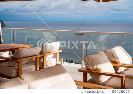 Restaurant with sea view. You can see rocks in the sea. Wooden tables and chairs with white cushions. Overcast, cloudy weather. Restaurant with sea view. You can see rocks in the sea. Wooden tables and chairs with white cushions. Overcast, cloudy weather. 89326065