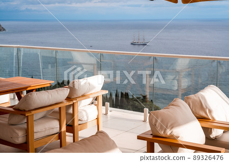 Restaurant with sea view. You can see rocks in the sea. Wooden tables and chairs with white cushions. Overcast, cloudy weather. Restaurant with sea view. You can see rocks in the sea. Wooden tables and chairs with white cushions. Overcast, cloudy weather. 89326476