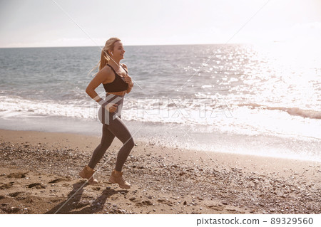 Happy young woman running along beautiful seashore Happy young woman running along beautiful seashore 89329560