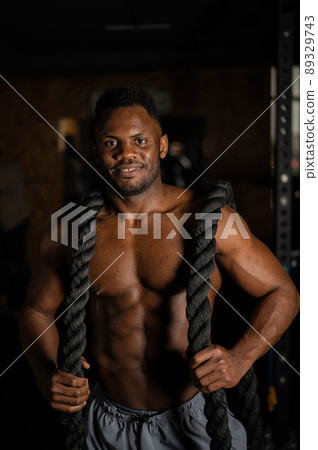 Muscular african american man posing with rope in gym.  89329743