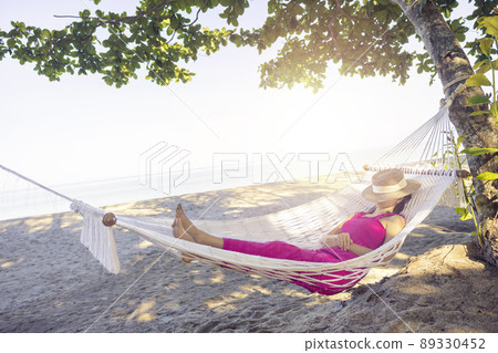Asian woman relaxing in the hammock on tropical beach, njoy her freedom and fresh air, wearing stylish hat and clothes. Happy smiling tourist in tropics in travel vacation 89330452