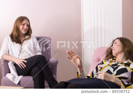 Young woman lying in the chair and talking to the psychologist sitting next to her at the doctor's office 89330752