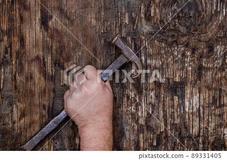 A man's left hand holds an old iron hammer against a dark wooden background. 89331405