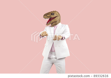 Strange guy in suit and funny dinosaur mask dancing against pink studio background 89332616