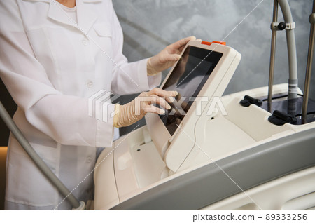 Close-up doctor hand on the screen monitor of a modern medical equipment, adjusting programs before treating patient in the clinic 89333256