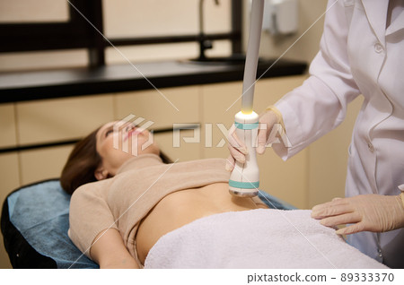 Close-up contact ultrasound sensor in the hand of a beautician giving cavitation body contouring, anti-cellulite slimming treatment in wellness spa 89333370