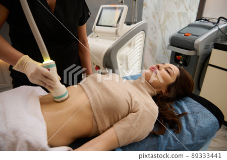 Charming woman receives anti-cellulite and anti-fat therapy in spa salon. Ultrasonic cavitation body contouring treatment Charming woman receives anti-cellulite and anti-fat therapy in spa salon. Ultrasonic cavitation body contouring treatment 89333441