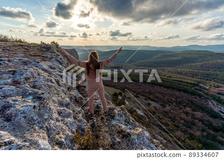 The girl at sunset. The girl stands with her back on the top of the mountain and looks at the sunset, welcomes the sun with her hands up, in Hampi. Meditation, alone with nature, silence. Hands up. The girl at sunset. The girl stands with her back on the top of the mountain and looks at the sunset, welcomes the sun with her hands up, in Hampi. Meditation, alone with nature, silence. Hands up. 89334607