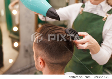 Hairdresser dries hair of stylish man. Young handsome guy doing hair styling at a hairdresser.. Hairdresser dries hair of stylish man. Young handsome guy doing hair styling at a hairdresser.. 89334670