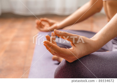 Young woman meditating in the lotus pose at home. Practicing yoga indoors. Harmony, yoga practice, balance, meditation, relaxation at home, healthy lifestyle concept. 89334672