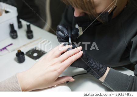 Manicurist applying gel polish on client's nails. Master of manicure in black gloves makes a french manicure on the nails of a woman. Manicurist applying gel polish on client's nails. Master of manicure in black gloves makes a french manicure on the nails of a woman. 89334953