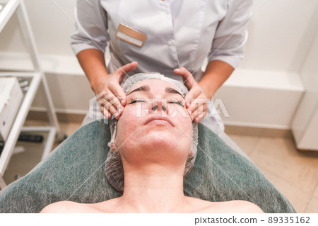 Doctor beautician makes cosmetic facial massage. Woman relaxes on a cosmetic chair side view.. Doctor beautician makes cosmetic facial massage. Woman relaxes on a cosmetic chair side view.. 89335162