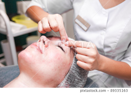 Doctor cosmetologist does facial cosmetology massage and massaging eyebrow area. 89335163