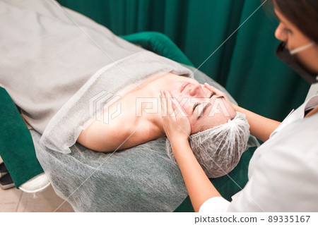 Doctor beautician makes cosmetic facial massage. Woman relaxes on a cosmetic chair.. 89335167