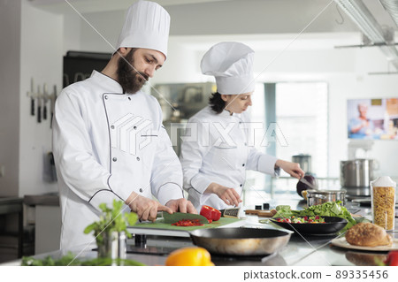 Skilled and confident head chef chopping organic and fresh red bell pepper while preparing garnish. Food industry worker cooking delicious gourmet dish for dinner service at restaurant. 89335456