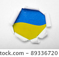 Ukrainian blue and yellow flag in the round hole in paper 89336720