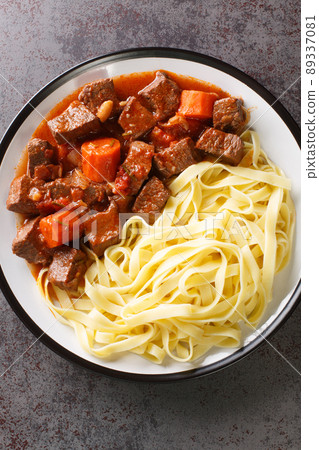Daube Provencal French braised beef red wine, and vegetable stew served with egg noodles closeup in the plate. Vertical top view Daube Provencal French braised beef red wine, and vegetable stew served with egg noodles closeup in the plate. Vertical top view 89337081
