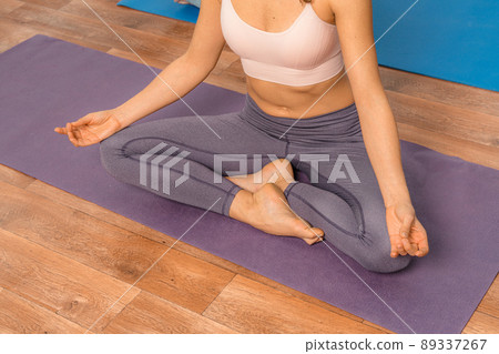 Young woman meditating in the lotus pose at home. Practicing yoga indoors. Harmony, yoga practice, balance, meditation, relaxation at home, healthy lifestyle concept. Young woman meditating in the lotus pose at home. Practicing yoga indoors. Harmony, yoga practice, balance, meditation, relaxation at home, healthy lifestyle concept. 89337267