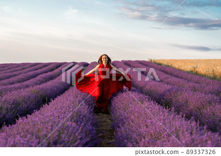 Among the lavender fields. A beautiful girl in a red dress runs against the background of a large lavender field 89337326