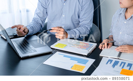 Two business colleagues pointing business data on laptop and taking notes information on notebook while reading 89338071