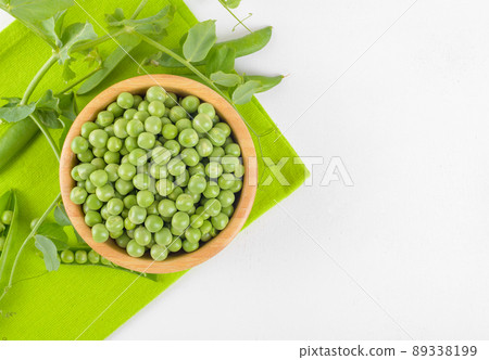Fresh green peas in a wooden bowl with peas plants leaves on napkin on white background, Healthy bean protein, top view 89338199