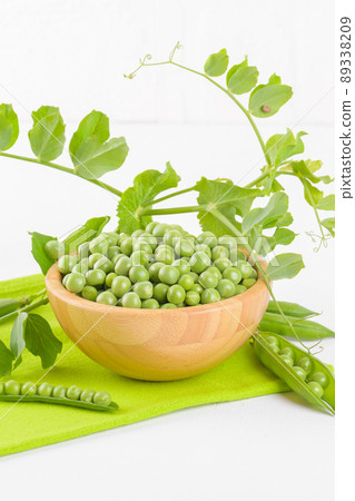 Fresh green peas in a wooden bowl with peas plants leaves on a green napkin on white background, Healthy bean protein Fresh green peas in a wooden bowl with peas plants leaves on a green napkin on white background, Healthy bean protein 89338209