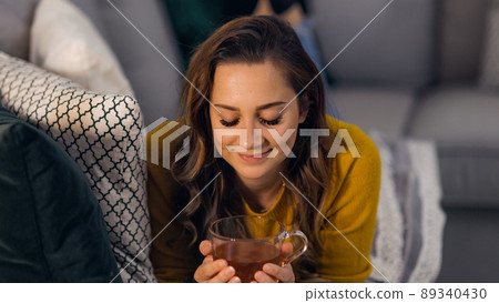 Young pretty woman drinks a cup of tea while lying on the couch 89340430