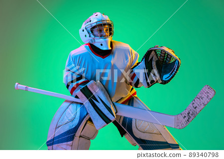 Dynamic portrait of teen boy, hockey player, goalkeeper catching puck with special glove isolated on green background in neon light Dynamic portrait of teen boy, hockey player, goalkeeper catching puck with special glove isolated on green background in neon light 89340798