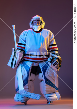 Portrait of boy, child posing in protective hockey uniform of goalkeeper isolated over purple background in neon light Portrait of boy, child posing in protective hockey uniform of goalkeeper isolated over purple background in neon light 89340836