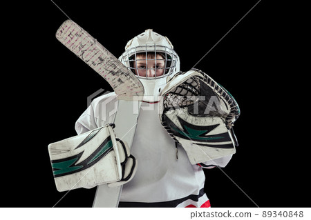 Portrait of boy, child in special protective uniform, in helment and gloves posing with hockey stick isolated over black studio background Portrait of boy, child in special protective uniform, in helment and gloves posing with hockey stick isolated over black studio background 89340848