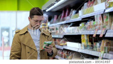Man chooses products in the grocery store, put it to the cart. Dairy products department. 89341497
