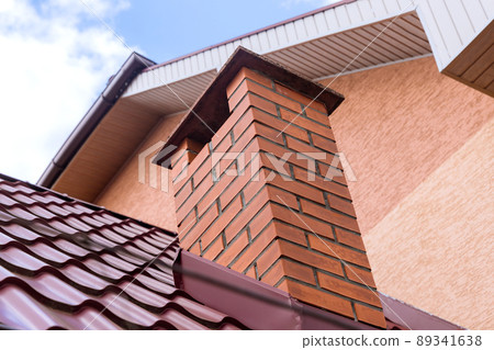 Chimney on the red metal tiles roof in of house against the blue sky Chimney on the red metal tiles roof in of house against the blue sky 89341638