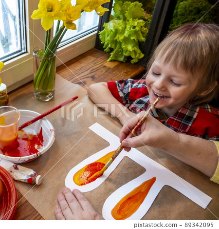 women's speckled hands teach boy drawing the ears of a handmade Easter bunny made of cardboard. Preparation for the celebration of the Easter holiday. 89342095