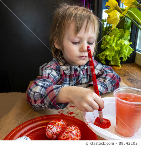 The child preparing for Easter. Paint eggs. Red paint egg. 89342102