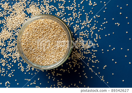 Raw quinoa in a glass jar and scattered grains over blue background. 89342627