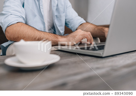 Hands of modern programmer or office manager over laptop keyboard under work on business plan. A guy in a blue shirt and white T-shirt. Cup of coffee on the table. Freelance 89343090