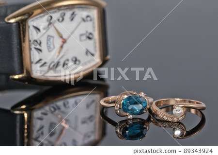 Pair of women's gold rings with diamonds on a background of elegant watches 89343924