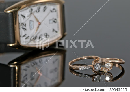 Pair of women's gold rings with diamonds on a background of elegant watches Pair of women's gold rings with diamonds on a background of elegant watches 89343925