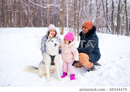 afro man with his caucasian wife having fun with a beautiful daughter playing husky in snowy park afro man with his caucasian wife having fun with a beautiful daughter playing husky in snowy park 89344479