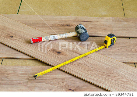 Metal measuring tape and rubber hammer on floor panels when laying them on the floor. 89344781