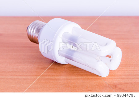 Compact fluorescent lamp on wooden table. 89344793