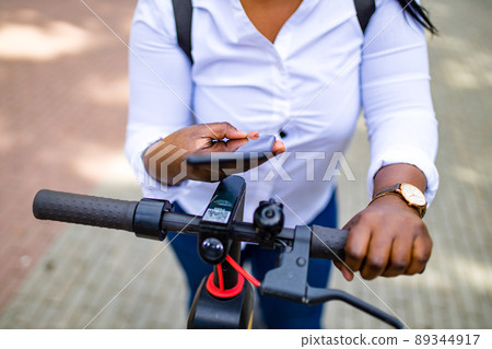 afro american woman activate and prepay a rental e-scooter or an e-bicycle on the street afro american woman activate and prepay a rental e-scooter or an e-bicycle on the street 89344917