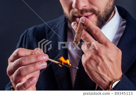 Portrait of an attractive business man with a cigar in black background studio 89345113