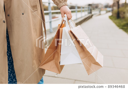 Cropped view of woman in autumn wear holding shopping paper bags in hands, walking at street, black friday. Urban lifestyle concept. Delivery carrying. Cropped view of woman in autumn wear holding shopping paper bags in hands, walking at street, black friday. Urban lifestyle concept. Delivery carrying. 89346468