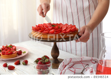 Woman in apron cut the strawberry tart Woman in apron cut the strawberry tart 89346514