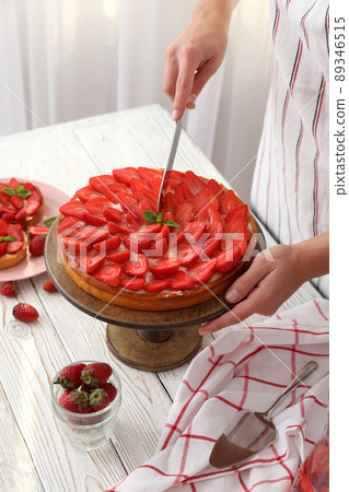 Woman in apron cut the strawberry tart Woman in apron cut the strawberry tart 89346515