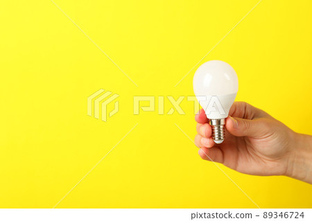 Female hand holds energy saving bulb on yellow background 89346724