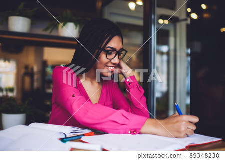 Smiling black female student doing homework in cafe 89348230