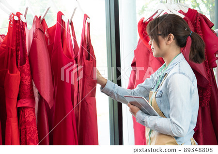 Happy young Asian woman dressmaker fashion designer is checking for completion for a suit and Dress in a showroom. Concept of success young entrepreneur in the fashion business. 89348808